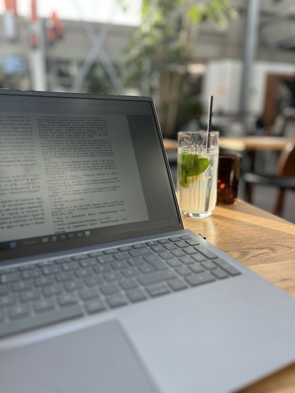 Ein Laptop mit geöffnetem Textdokument steht auf einem Tisch, daneben ein Glas Limonade