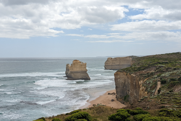 View from a wooden platform on the cliff-top at the official end of the hike, Great Ocean Walk, Victoria, Australia. On the right of the photo, the rugged coastline is defined by a sheer vertical cliff. In the centre is one of the columnar rock formations that's part of the Twelve Apostles. It's an intensely sunny day with bright blue sky and streaky white clouds. On the left, the blue-green sea rolls in. The powerful wind here is telling you that far off the left edge of the photo, over thousands of uninterrupted kilometres of sea, is Antarctica.