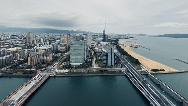 Skyline of Fukuoka as seen from the 29th floor of a hotel, a wide river flows in the foreground with the sea to the right.