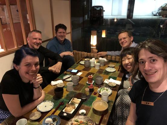 Six people at a restaurant table enjoying drinks and small plates of food