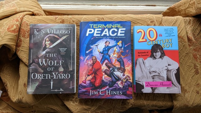 Three hardcover books face up on a shelf - The Wolf of Oren-Yaro by K.S. Villoso, Terminal Peace by Jim C. Hines, and 20th Century Boy by Duncan Hannah.