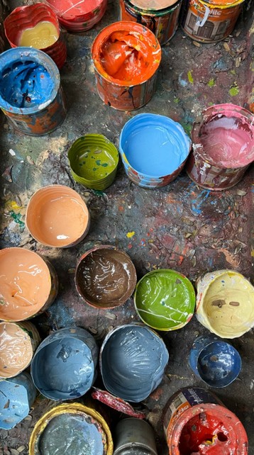 On a gray tray are many enamel paints (in various colours) all in half cut water bottles