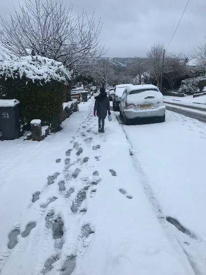 A little girl walking to school in the snow, along a pavement.