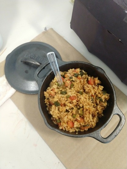 Picture of a small black pot full of rice with tomatoes and chili peppers
