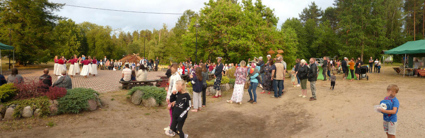 Image panoramique : parc arboré, premier plan dégagé, un groupe de danseuses donne un spectacle sur une cour en autobloquants, des gens regardent vaguement, des enfants jouent.