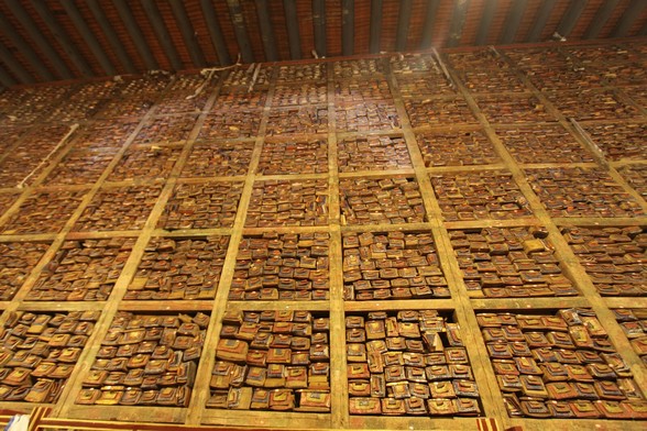 Looking up at a very tall wall of books/scrolls inside of small boxes which are grouped inside of cubes. Everything is mostly brown with splashes of bright colors.
