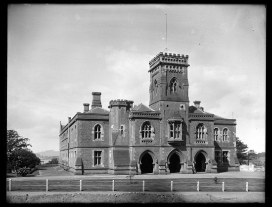 Black-and-white photo: Supreme Court, Waterloo Quadrant, Auckland Central, 1921. Photographer, Henry Winkelmann (1860–1931). Front view of the Supreme Court on Waterloo Quadrant between Parliament Street and Anzac Avenue, with a glimpse of the harbour and Rangitoto in the background. The Supreme Court was renamed as the High Court in 1980. Auckland Libraries Heritage Collections 1-W1724. https://kura.aucklandlibraries.govt.nz/digital/collection/photos/id/97846