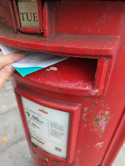 Photograph of an envelope being posted into a red Royal mail post box