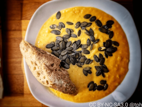 Die fertige Kürbissuppe auf einem weißen Teller mit Kürbisskernen und Baguette angerichtet.