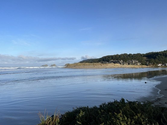 High tide at Cannon Beach— Ecola Creek’s outflow to the ocean is subsumed by the incoming tide, and the ocean splashes in the distance at the base of the headland.