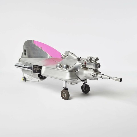 A machine, or assemblage, made from aluminium, chrome plated metal, perspex, iron, rubber, enamel paint. It looks like a mix between a Formula 1 car and jet plane. Two wheels on the front, one in the back. On its side is a nameplate with 'Tajiri' as well as a large number '8' on its tail. The front part of the tail has a bright pink colour. This is Shinkichi Tajiri's 'Number 8', made in 1968.