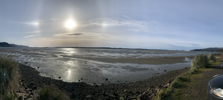 Panorama of Netarts Bay, OR at the start of low tide. It is sometime around 4:15 and the sun displays a halo above Netarts Spit. Sandbars are beginning to be revealed as the tide recedes.