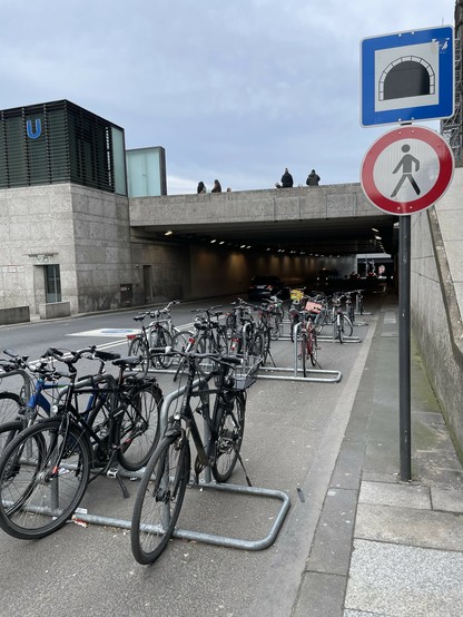 Fahrradständer vor einem Tunnel, rechts ein Schild dem gemäß der Durchgang für Fußgänger verboten ist