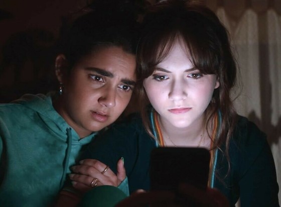 Geraldine Viswanathan and Emilia Jones are head to head staring at a computer screen.