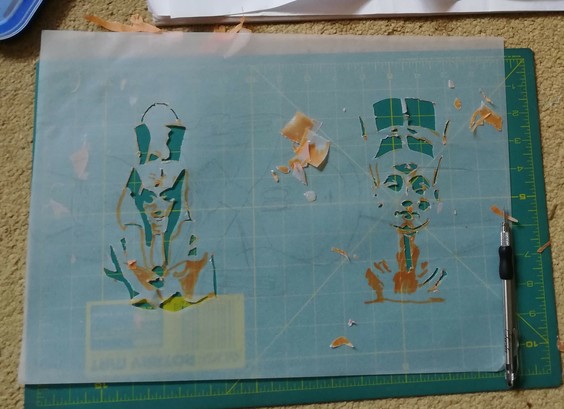 A piece of tracing paper lies on a green cutting mat. Stencils of Akhenaten and Nefertiti are partially prepared.
