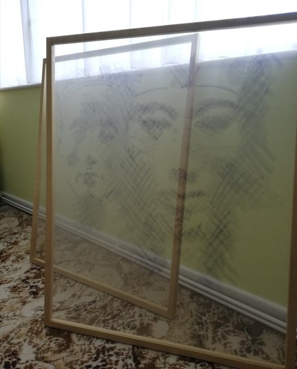 Faces of Akhenaten and Nefertiti painted on gauze stretched over frames, leaning on a wall under a window.