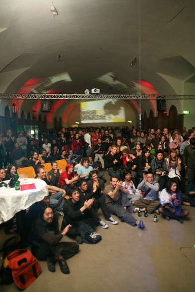 Why PK (Pecha Kucha) is OK: photograph of an enthusiastic sitting and standing audience listening to a set of Pecha Kucha talks in a hall with a curved buttress ceiling