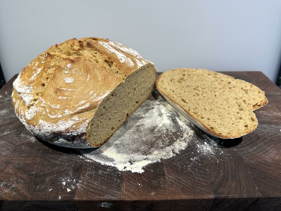 A round loaf of khorasan sourdough bread with two slices cut off on a maple cutting board.