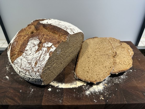 A round khorasan sourdough bread on a cutting board with 3 slices cut off lying to the side.