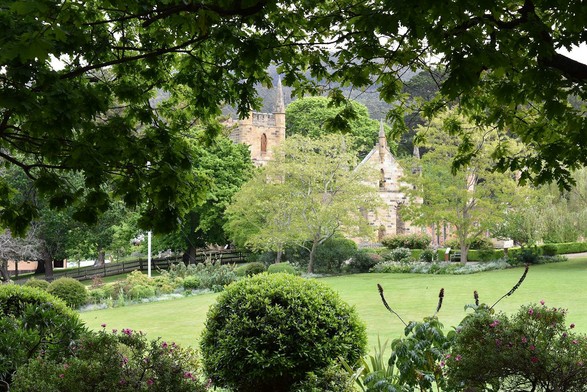 Trees, bushes and flower beds surrounding a lawn. In the background, behind trees, is a stone church (actually, just the walls of church).