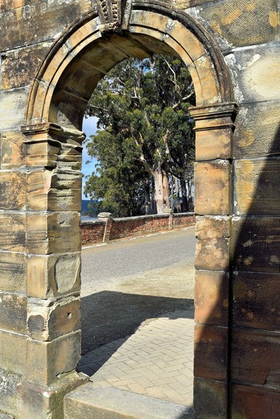 This is the far arch in the other photo. At a different angle, so through the arch can be seen the road (bitumen) bordered by a low wall of orange brick, and gum trees beyond that.