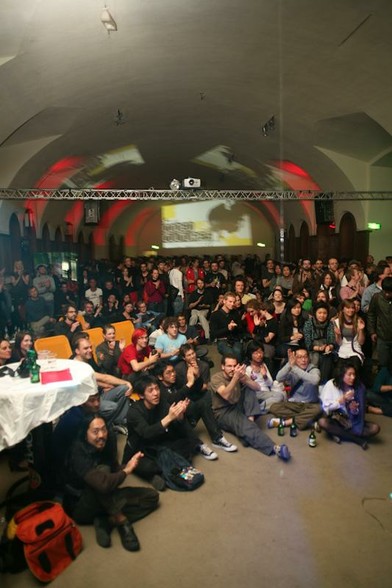 Why PK (Pecha Kucha) is OK: photograph of an enthusiastic sitting and standing audience listening to a set of Pecha Kucha talks in a hall with a curved buttress ceiling