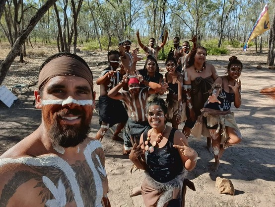On country First Nations Wangan people with “painted” white art on faces and bodies smile for camera.