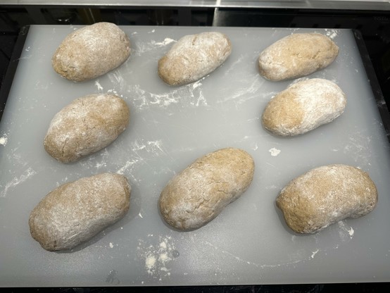 Eight pieces of dough for bread rolls proofing on a board.