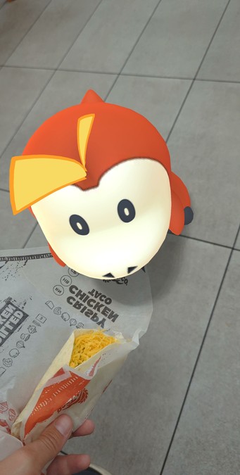 A top down Pokémon GO AR photograph of Fuecoco being offered a fast-food taco.