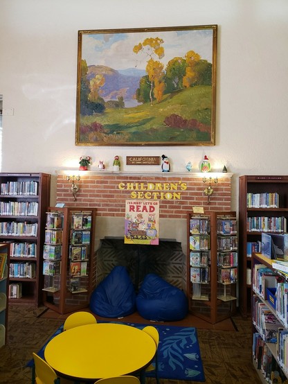 White plaster wall above brick fireplace and children's seating and bookcases. Large beautiful landscape painting of hills and trees and ocean by Dana Bartlett ❤
