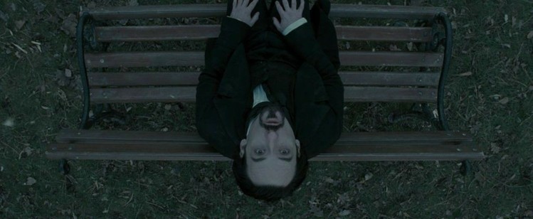 A dark-haired man tilts his head back on a bench, looking straight up into the sky