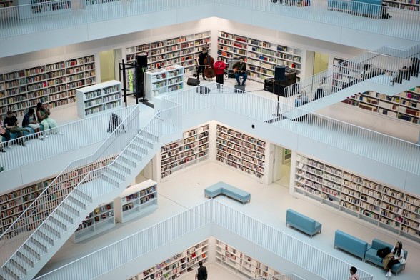 Ein großer, mehrgeschossige, vornehmlich in weiß gehaltener Lesesaal. An den Wänden rundherum Bücherregal. In der Ecke auf einer der Galerien spielt eine dreiköpfige Band. Die Sängerin trägt rote Kleidung.