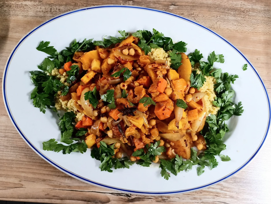 Auf einer Servierplatte Couscous, darauf das Gemüse, mit Petersilie umgeben.