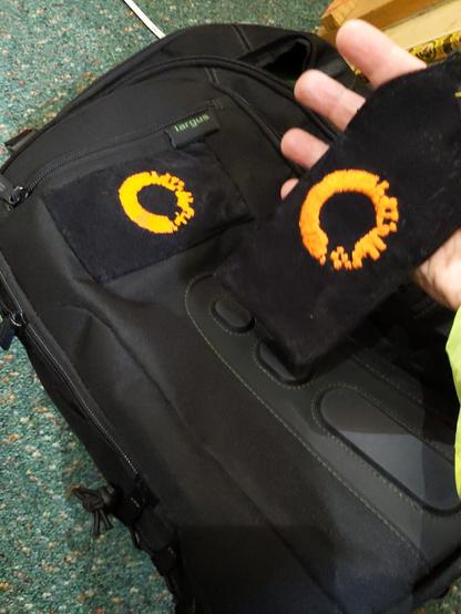 A backpack and badge holder embroidered with a pixelated orange ring logo image.