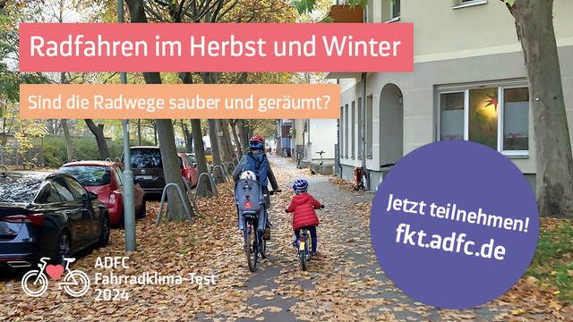 Familie auf Fahrrädern auf einem mit Laub bedeckten Radweg in einer Stadt zwischen parkenden Autos und einer Hausfassade.