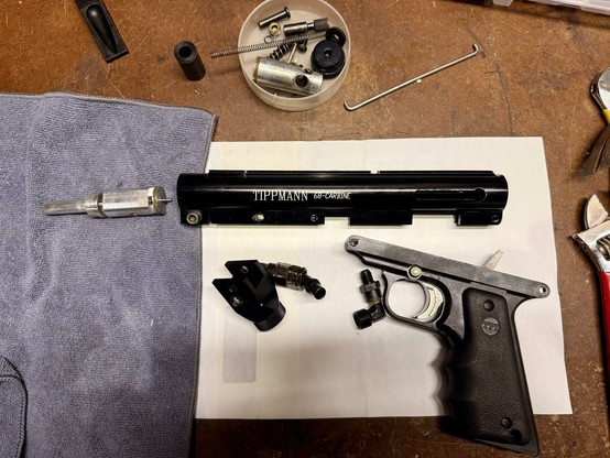 A black Tippmann 68 Carbine paintball gun fully disassembled on a workbench