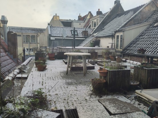 Photo of a roof terrace with planters, table and pots, surrounded by other roofs, covered in a little snow.