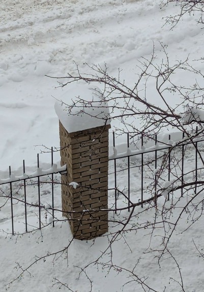 A thick cap of snow sits atop a brick fence post