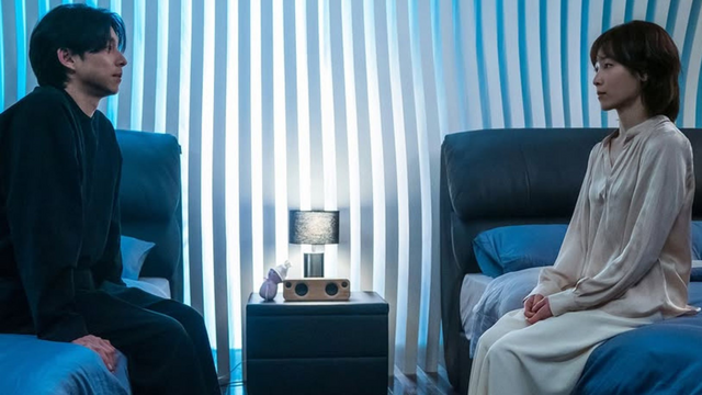 Gong Yoo & Seo Hyun Jin from a scene in the 2024 South Korean drama "The Trunk" sitting on 2 beds facing each other.