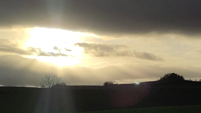 Hegaulandschaft mit Bergen als dunkle Kulisse. Die Sonne bricht durch die Wolken und es entstehen sichtbare Lichtstrahlen.