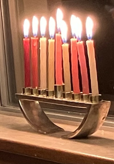 A basic menorah, sitting on a windowsill, with all candles lit for the last night of Chanukah