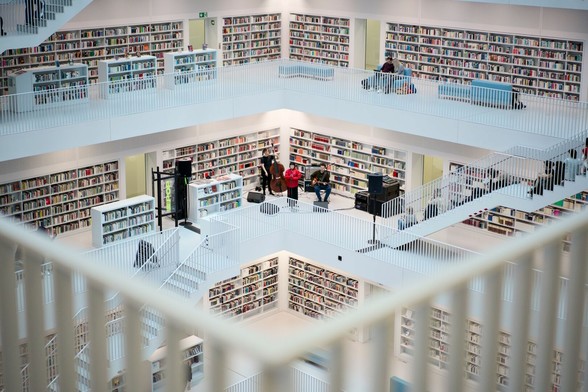 Ein Blick in den Lesesaal, der komplett in Weiß gehalten ist. Die Galerien sind rundherum mit Bücherregalen versehen. In der Ecke einer Galerie steht eine Band mit einer Sängerin in knallroter Kleidung. Im Vordergrund unscharf ein Geländer.