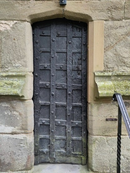 An ancient iron clad wooden door. It's painted black and the surround is stonework.