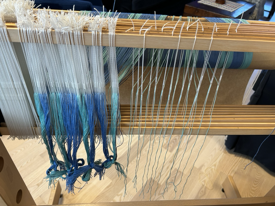 A series of threaded heddles garhered in groups with individual threaded heddles to the right showing the threading pattern on 4 shafts of a hand loom
