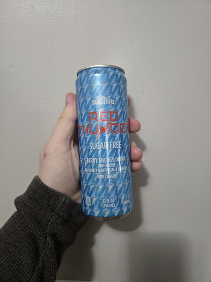Photograph of a white person's hand holding a light blue can against a light colored wall. The can is labeled Summit Red Thunder Sugar Free. It is Aldi's version of sugar free Red Bull.