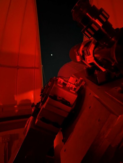 The interior of an astronomy dome, showing a telescope aimed at Venus (visible through an opening in the dome, no telescope required).