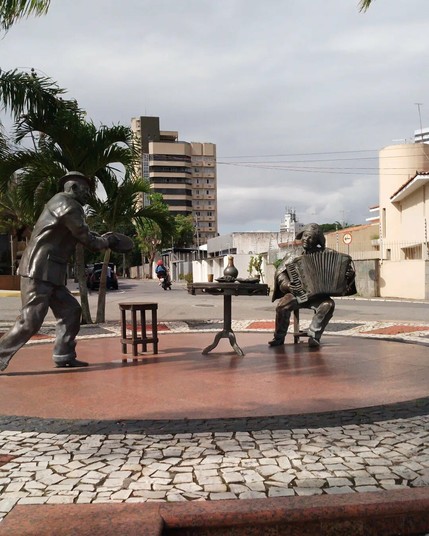 Duas estátuas de metal cinzento de duas pessoas em tamanho real. Um deles está em pé e toca um pandeiro e representa o artista paraibano Jackson do Pandeiro. O outro, Luís Gonzaga, está sentado e toca sanfona. Estão separados um do outro por uma mesa de bar.