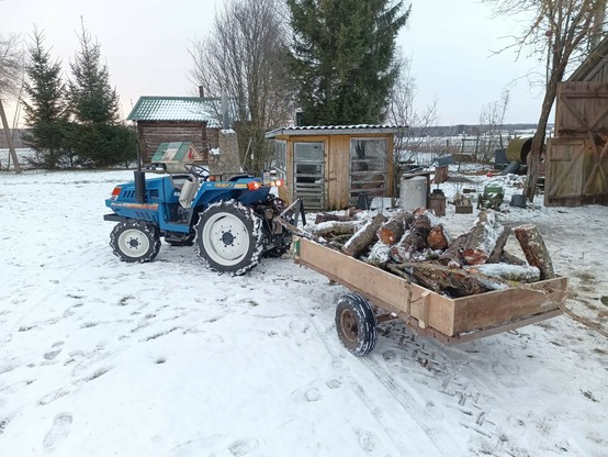 Tractor and trailer again. Now fully laden with logs from fallen trees and some snow, they are parked in front of a barn for unloading.