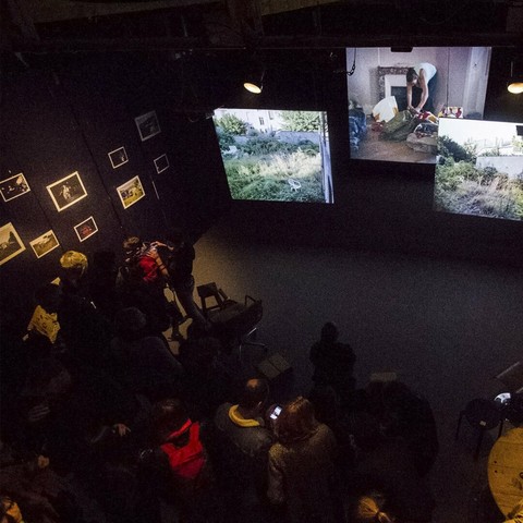 Exposition de ZONE 54 : I love You Fuck Off, au CCGP (Nancy). Triple vidéoprojection synchronisée. Ici une vue du dessus de l'installation, in grand écran (3x4m) au fond, deux écrans plus petits suspendu plusieurs mètres devant. Au premier plan de nombreuses personnes, c'est le jour du vernissage.