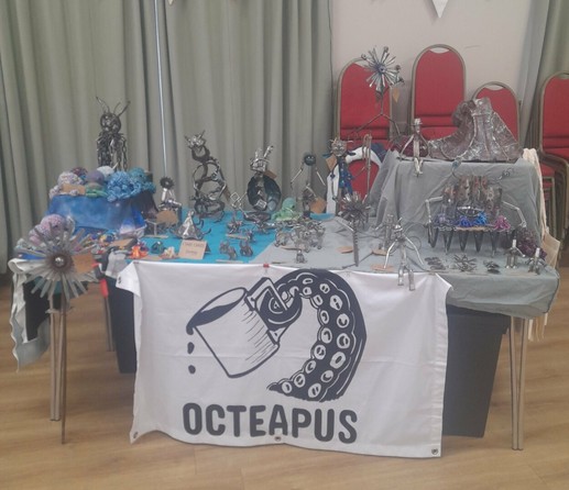 OcTeaPus stall, a table with lots of metal work on plus crocheted octopuses in a village hall